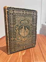 Front angled view of ornate green and gold embossed hardcover book
