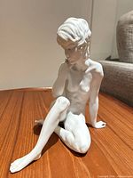Front three-quarter view of white porcelain seated boy figurine on wooden surface