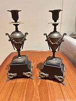 Full view of both matching bronze candlestick holders on black bases