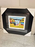 Framed Maud Lewis print with protective corners on couch