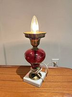 Lamp front view showing marble base, red glass body, brass collar, flame bulb lit