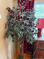 Full view of artificial tree in corner showing foliage, braided trunk, pot, and string lights
