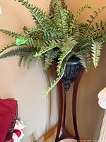 Full view showing artificial fern in urn planter on tall wood pedestal