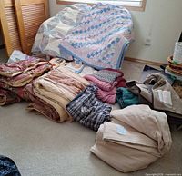 Entire assortment of folded blankets, quilt, throws and jacket on floor and chair
