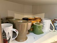 Cupboard shelf showing assorted mugs: beige, speckled, green, white with text, brown, printed London design