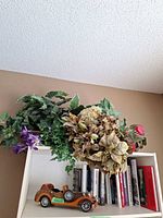 Overall view showing floral arrangement atop shelf, wooden model car and books below