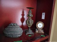 Three ornate resin pieces: clock, candlestick, lidded box on shelf