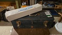 Closed blue steel toolbox with rust, grease gun box resting on top