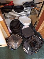 Full lot on shelving: electric skillet, grill plates, enamel roaster, stacked pans