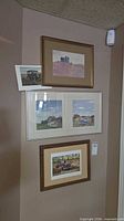 Four framed prints arranged on wall including truck scene, triptych coastal scene, house on hill and small car print