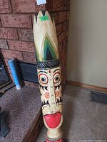 Full view of carved wood tiki statue leaning against fireplace