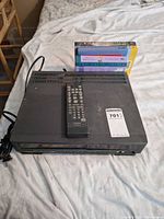 VCR with remote on top, power cord coiled, books behind