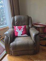 Front view of brown leather recliner with pillow placed for scale, shows wear on seat and arms