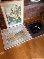 Three framed artworks laid out: watercolor town scene, pastel house sketch, space photographic print