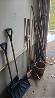 Group of long-handled tools, bucket and hooks leaning against garage wall