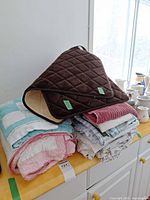 Stack of quilts and linens with folded brown quilted mat on top