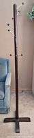 Full view of tall wooden coat rack beside chair