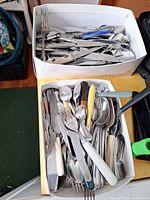 Two boxes filled with mixed knives, forks, spoons