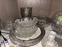 Mixed glassware stacked inside cabinet; shows pitcher, bowls, charger, relish dish
