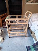 Three-quarter front view of rattan bar cart showing handle, two glass shelves and casters