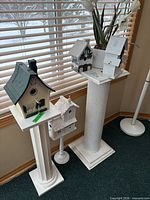 Four white plant stands with birdhouse decorations displayed by window