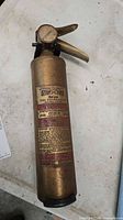 Full view of brass Stop-Fire extinguisher showing body, handle and base