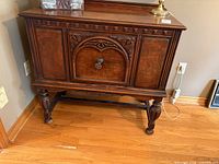 Front view of mahogany veneer sideboard showing carved door, turned legs, veneer grain