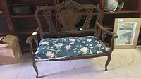 Front view of carved wood loveseat with floral cushion