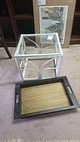 Square white rattan side table with clear glass top and separate wooden tray placed in front