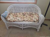 Front view of white wicker loveseat with floral cushion and decorative pillow