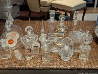 Group of approximately eighteen clear and frosted crystal perfume bottles on tabletop
