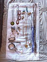 Full assortment of jewellery laid out on towel, multiple necklaces, bracelets, earrings, rings visible