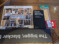 Overview showing Friends puzzle, CAH base game, wooden scorekeeper, playing-card deck, edge of bigger blacker box