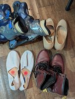 Five pairs of shoes on wooden floor: Fluevog booties, beige flats, Verbenas espadrilles, Comanchero boots, partial view of other pair