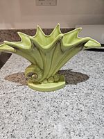 Full side view of green drip glaze snail shell vase on counter