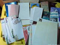 Assorted writing pads, envelopes, blank paper on yellow bin lid
