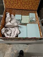 Open patterned box showing multiple light blue Partylite boxes, packing paper, clear glass holder