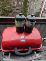Red Backyard Grill tabletop propane grill with two green propane cylinders seated on lid