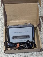 USB cassette capture device in open cardboard box with USB cable and earphones visible