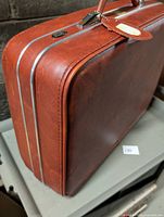 Side view showing reddish-brown hard-sided suitcase, aluminum trim, handle, luggage tag and keys