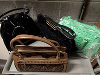 Four handbags grouped: brown tooled leather, black patent, black velvet, green studded