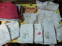 Group view of embroidered pillowcases, crochet doilies, crochet tablecloth, red and grey linens