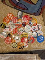 Spread of pins laid out on chair showing variety of slogans, colours and shapes