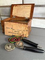 open oak box showing instruction label and disc electrodes with leads and hand grips