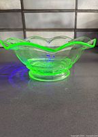 Bowl glowing bright green under UV light, showing ruffled rim and footed base