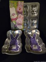 Three aluminum bunny cake pans displayed, two full-body pans and one six-cavity pan, with packaging insert visible