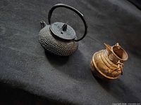 Cast iron teapot and copper pitcher side by side on black fabric