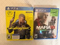 Front view of two sealed PS4 game cases: Cyberpunk 2077 and Mafia III