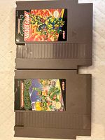 Front view of two NES cartridges showing label art for TMNT and TMNT II