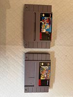 Two SNES cartridges front view showing labels for identification: Looney Tunes B-Ball and Mario Paint